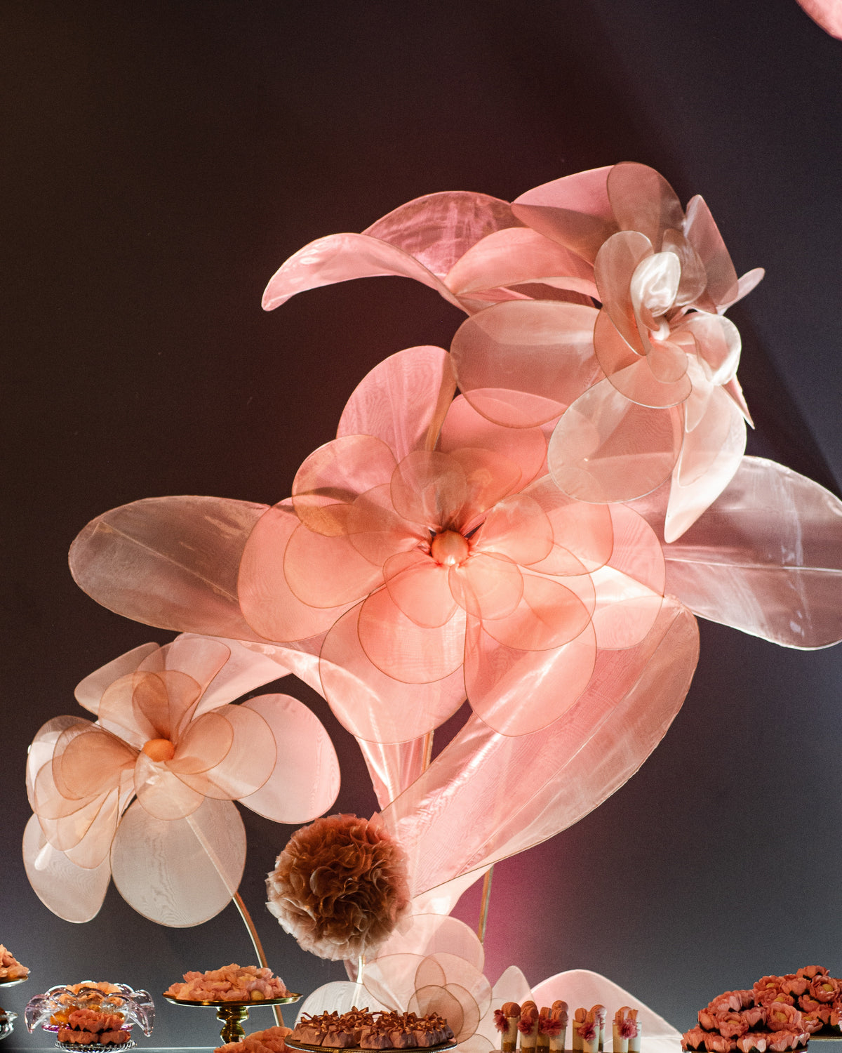 Sculpture de fleurs géantes en organza rosé, sur la table de desserts d'une fête