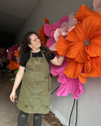 Flores gigantes de crepom italiano em pedestal ao lado da designer Jacqueline Benevides, mostrando a escala