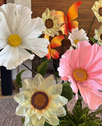 Camomila gigante de papel crepom rosa, no jardim de um batizado, com outras flores gigantes