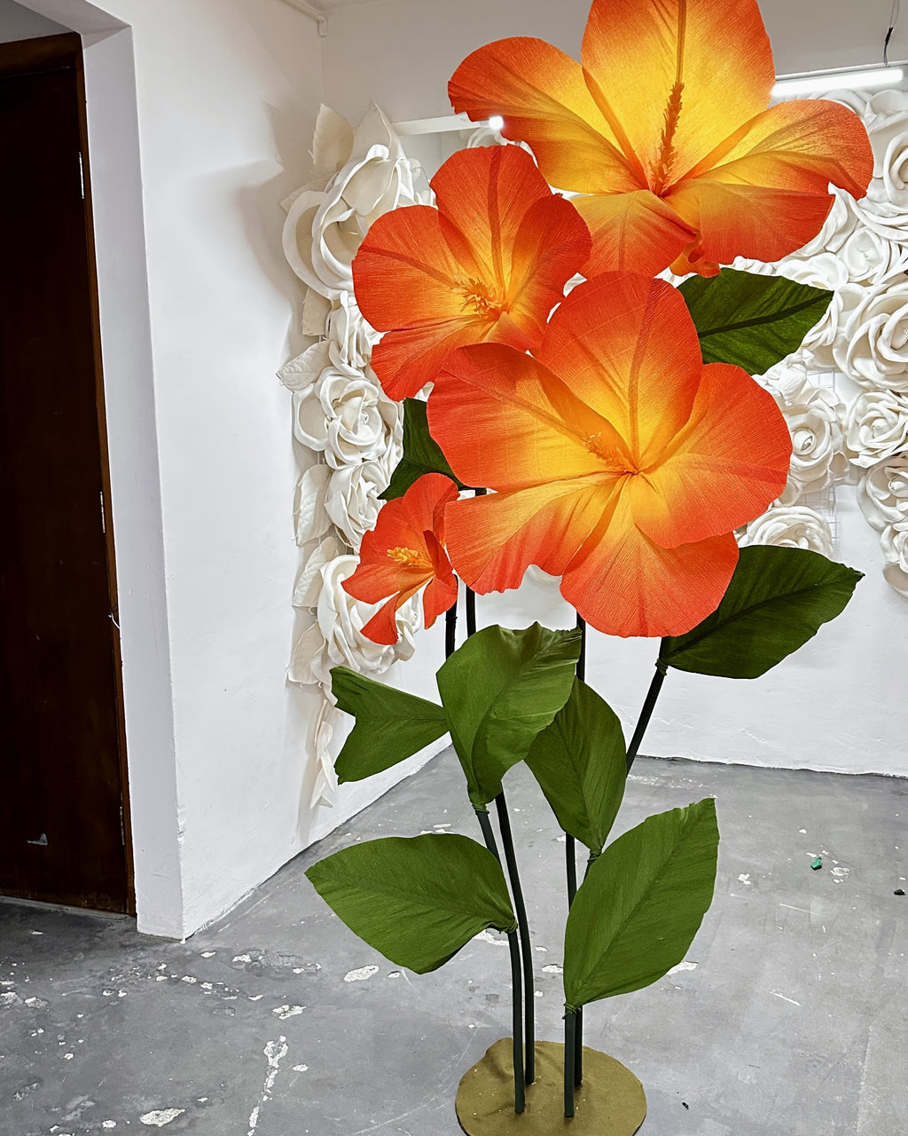 Hibiscos gigantes de papel crepom laranja em pedestal com folhas