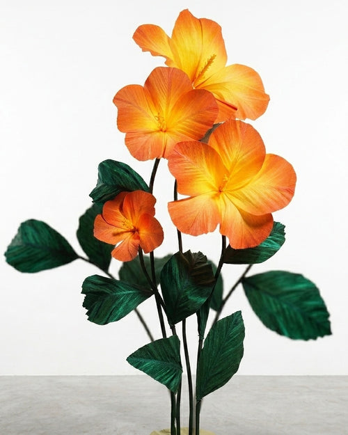 Pedestal com hibiscos gigantes de papel crepom italiano em degradê laranja e folhagem verde